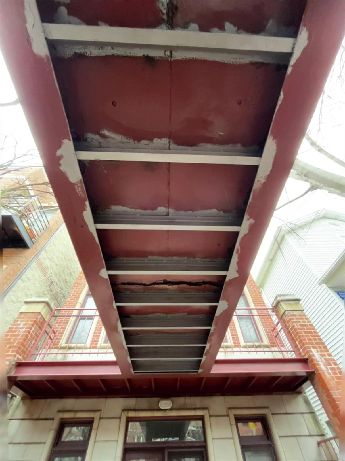 Underside of a steel porch mid-repair, primed steel with fresh structural patches