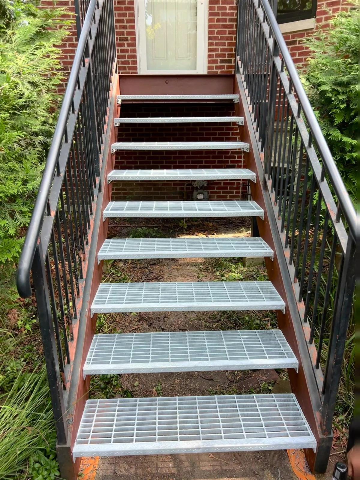 New galvanized steel bar-grating stair treads installed on a steel porch — the zinc coating shines silver